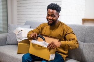African-American man sitting comfortably in living room and unboxing package with joy after receiving online shopping delivery