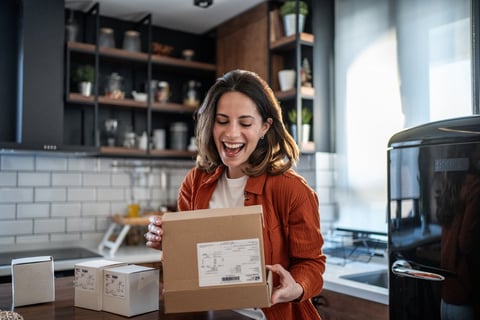 Happy young woman unboxing a delivery package in a modern kitchen