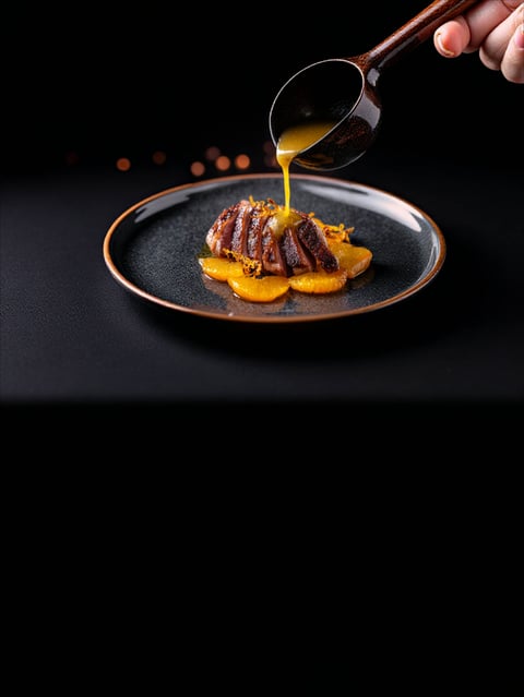Sliced duck breast with orange sauce being poured from a wooden ladle