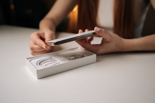 Cropped shot of woman unboxing modern smartphone, revealing sleek device on minimalist white table
