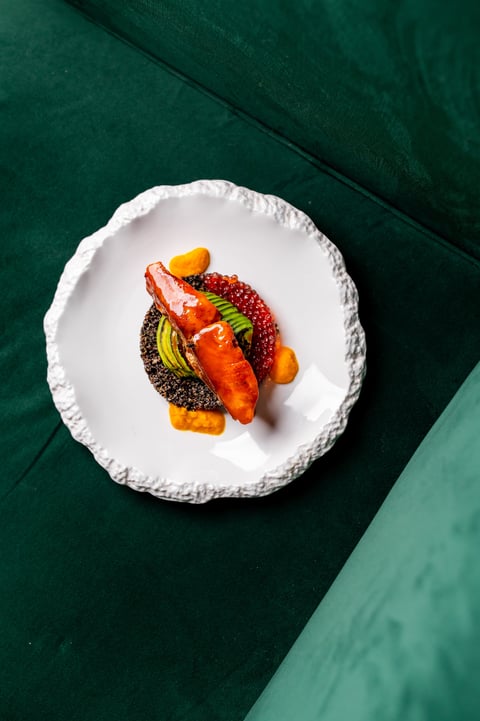Gourmet dish with plated salmon, red caviar, avocado, and sauce on a modern white plate